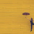 woman happily jumping with umbrella, yellow backgound