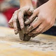 Hands shaping clay on a wooden table.