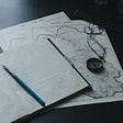 on a table there are maps, a compass, a journal full of writing, and a blue fountain pen sitting between the open pages