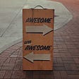 Sign on a pavement with the word “awesome” above an arrow pointing to the right, and the words “less awesome” above an arrow
