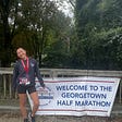 me, post race, standing in front of a banner that reads “WELCOME TO THE GEORGETOWN HALF MARATHON”