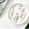 a white plate of white pills on white background with two green leaves on the side