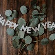 Happy New Year sign over eucalyptus branch on wooden table.