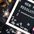 black background with new years eve sparklers and board new years Eve resolutions held by lady’s hand with red painted nails