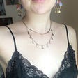 Woman wearing lacy black slip dress with layered gold necklace and statement earrings