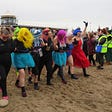 A group in fancy dress striding down a beach ready to throw themselves in the sea for charity on New Year’s Day.