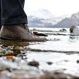 Hiking boots in icy water at a lakeside.