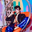 A person wearing colorful makeup and a glittery outfit making a phone call.