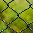 close-up of a chain link fence with a blurry grassy background