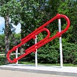 a giant red paperclip on a stand in a park
