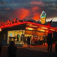 An ice cream stand in a small town with neon and a sunset. Small Town Rain by Jim Latham