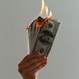 Picture of white hand holding American dollars that are on fire.
