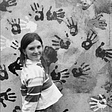 Emerging curator Poppy Thomson standing outside Berlin’s East Side Gallery. Thomson is pictured standing side on, face turned towards the camera. She stands in front of a wall covered with hand prints