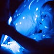 Little girl in bed at night, holding a device, which emits blue light.