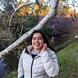 Dani Solis stands on a grassy hill by a tree, smiling.