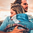 couple wearing denim jackets hugging each other sunset sky behind them