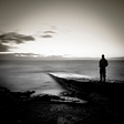 black and white a man in silhouette standing with hands in pocket on the edge of a rocky precipice looking out at the sea and the sky garrulous glaswegian medium
