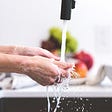 person washing hands at kitchen sink