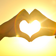 Girl’s hands in a heart shape above her head with the sun shining brightly in the middle.