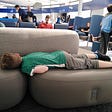 A child laid out fast asleep on seats by an airport departure gate