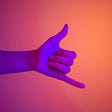 Gradient background in purples to oragne tones. Hand stretching across making the hang loose sign