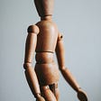 A close up of a hardwood manikin against an off white background.