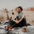 Couple sitting on a blanket holding hands in a desolate landscape. Adam Murauskas. FixYourPicker.com. Relationship Coach. Dating Coach. Anxious attachment. Attachment style.
