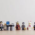 Four Lego figures — an ancient Mongolian warrior, a zombie in a suit, a guy in a bunny costume and a skeleton in a black suit and a derby — line up for a job interview with a stressed Lego man in a suit.