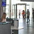 Image of ground-floor reception desk staffed by a young woman who is seated within a modern, clean and busy lobby area of a building.