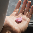 A heart-shaped pink color pill that has “feelings” written on it, in a palm of a man’s hand