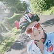A woman smiling wearing a cycling helmet on a cycling path bathed in sunshine
