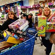 Two women in store with hands and shopping carts overloaded with toys on a Black Friday shopping day.