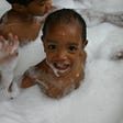 Baby Nathan waving in his bubble bath as a one year old baby