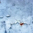 White plaster, interspersed with red rusty blotches, peeling off an exterior wall.