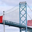 An image of a bridge joing Canada and the USA with both country’s flags flying.