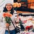 Woman holding a cup of takeout coffee and bouquet of orange flowers at farmers market