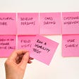 7 pink post-its on a wall with a hand holding one that reads: Run a usability test.