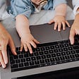 A close-up of a mother and baby’s hands on a laptop