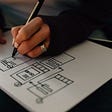 A User Interface (UI) Designer sketches a design for an app on paper with a black pen