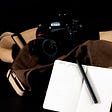 A display of a camera bag, camera with lens attached, and a pocket notebook with fountain pen for note taking duties. Oberhausen, Germany, September 24, 2022.