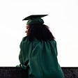 A black woman in a green graduation cap and gown