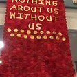 A banner made up of hundred of individually stitched red hexagons. In gold writting over the top it says Nothing About Us Without Us