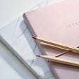 Two pencils with pink tips sit on top of a pink journal with the words JOURNAL written in the middle.