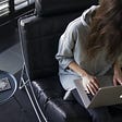 woman in blue chambray long-sleeved top sitting on black leather chair with silver MacBook on lap