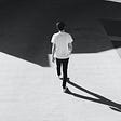 Person walking on concrete road, towards a shadow, image black and white