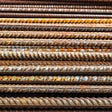 A section of approximately fifteen construction rebar, metal, cylindrical bars, in varying degrees of rust, lined up on top of each other.