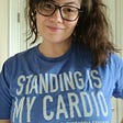 Image of author, Nicole, from the waist up with one hand across her stomach and the other on her hip, wearing a shirt that says ‘Standing is my cardio Postural Orthostatic Tachycardia Syndrome.’