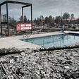 Destruction around a swimming pool in the wake of a weather event. A red sign reads “WE WILL REBUILD.”