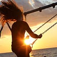 Image of a woman riding a swing at sunset