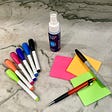 Dry erase markers and cleaner, sticky notes, a marker, and a mechanical pencil arranged on a stone background